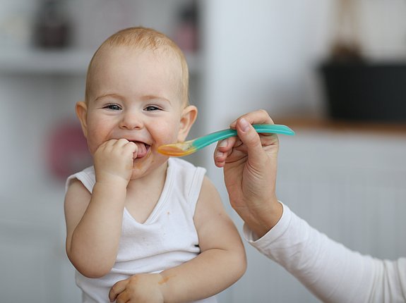 Lachendes Baby wird mit Babybrei gefüttert