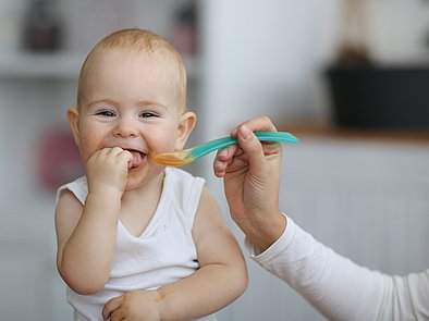 Lachendes Baby wird mit Babybrei gefüttert