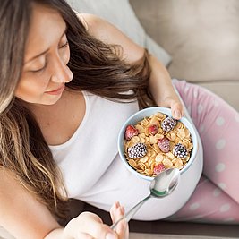 Schwangere Frau isst gesunde Müsli-Bowl mit Beeren