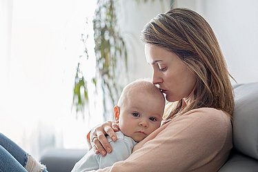 Liebevolle Körpernähe und Geduld sind gerade in schwierigen Phasen hilfreich. Mutter küsst liebevoll trauriges Baby.