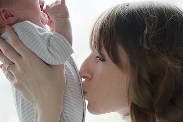 Mutter küsst schreiendes Baby liebevoll auf den Bauch