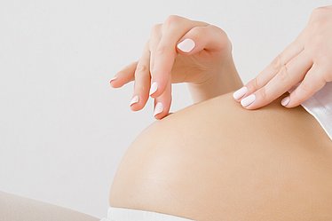 Schwangere streichelt sanft über ihren Babybauch