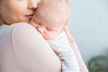 Mutter trägt schlafendes Baby eng am Körper.