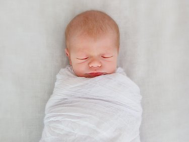 Baby eng eingewickelt (gepuckt) in ein weißes Tuch.