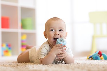 fröhliches Baby auf dem Bauch liegend mit Fläschchen in der Hand