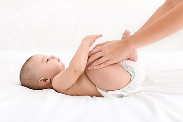 Mutter schiebt Beine des Babys in Richtung Oberkörper