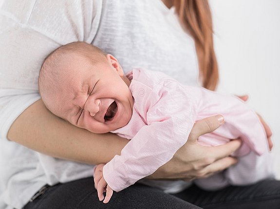 Frau trägt Baby im Fliegergriff