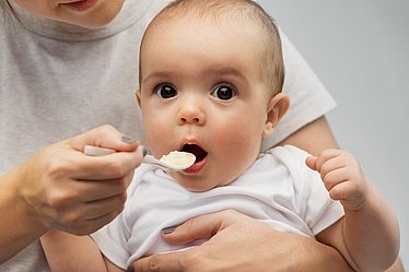 Mutter füttert Baby behutsam mit Brei.