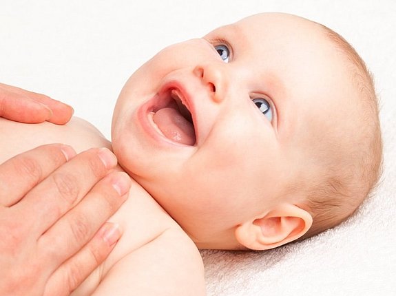 Baby liegt glücklich auf dem Rücken und wird am Bauch massiert