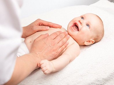 Baby liegt glücklich auf dem Rücken und wird am Bauch massiert